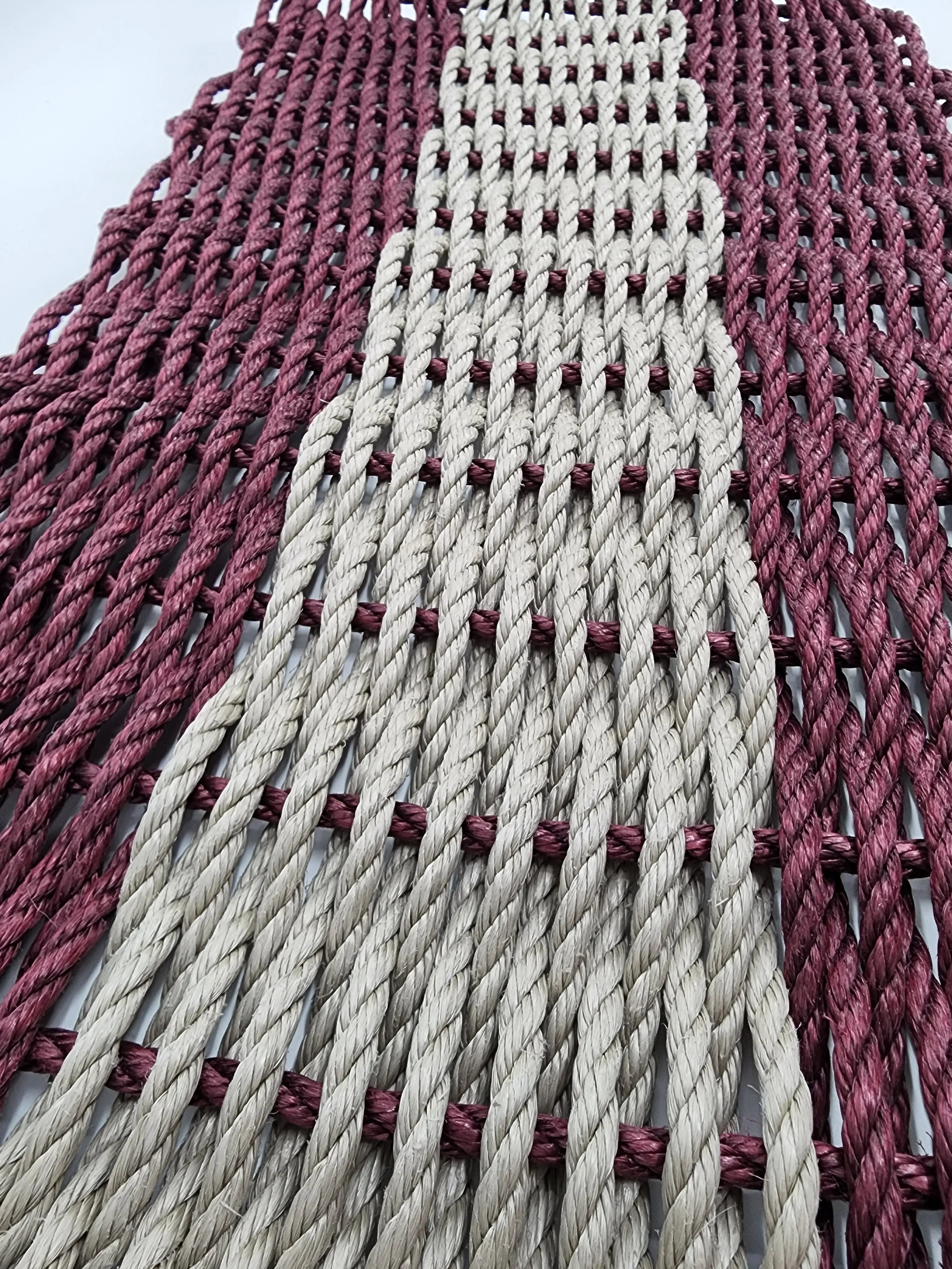 Burgundy and tan handmade lobster rope mat on wooden floor