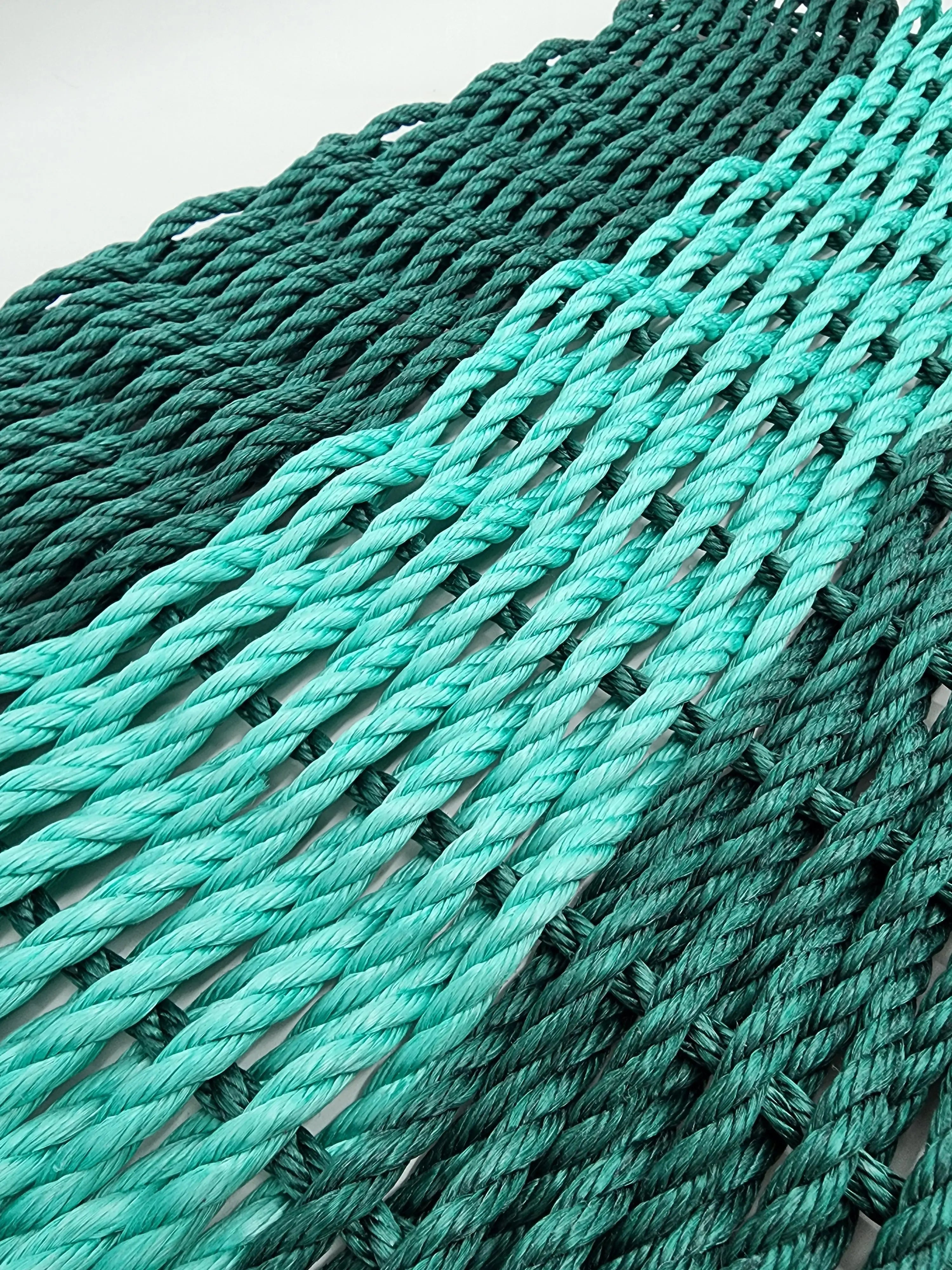 Hunter green and teal handmade lobster rope mat on wooden floor