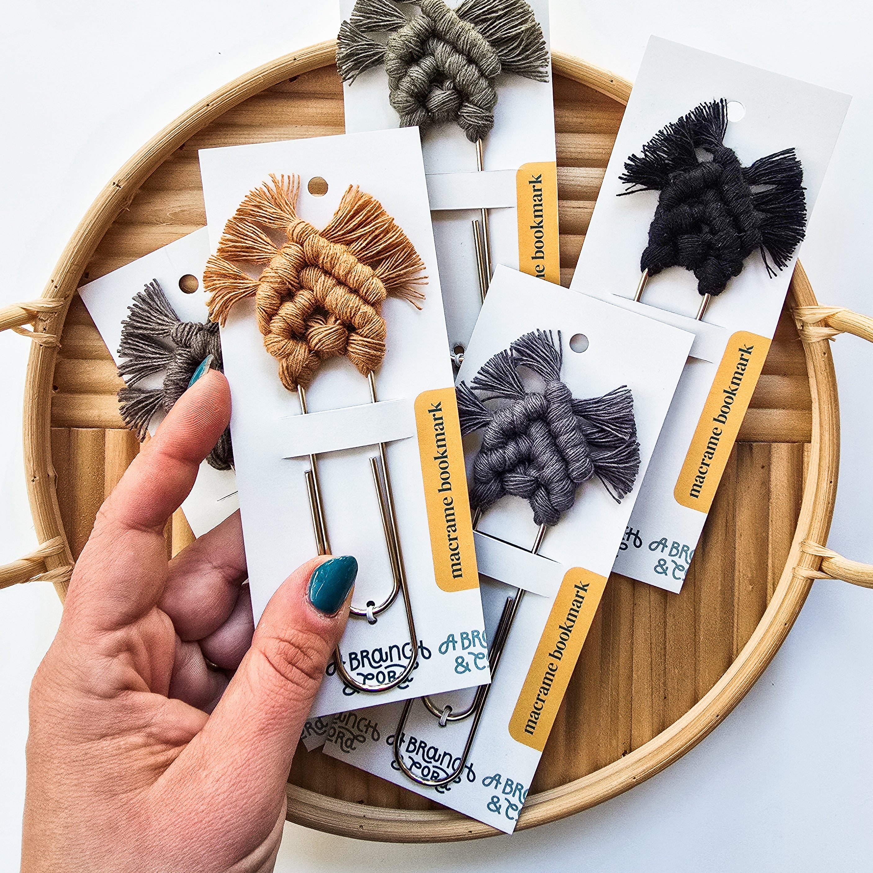 Neutral-toned macrame bookmarks laid out on a wooden surface with book edges visible