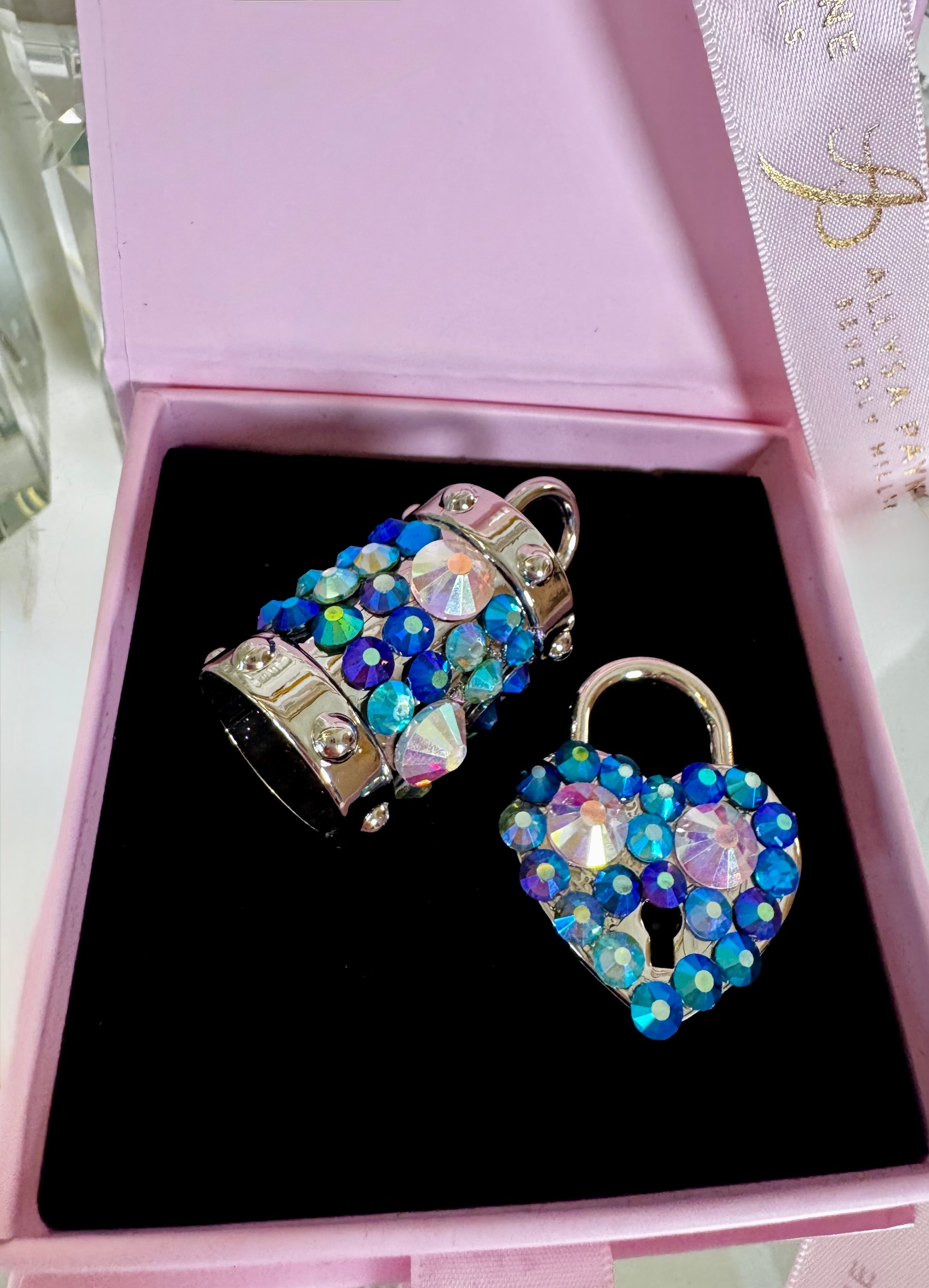 Blue Swarovski Crystal Love Charm Set with heart locket and bell charm on a dark fabric background.