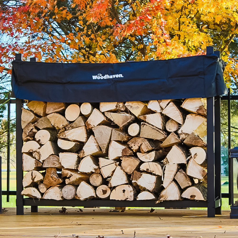 The Woodhaven 5 ft Firewood Rack in black showing stacked firewood on a patio