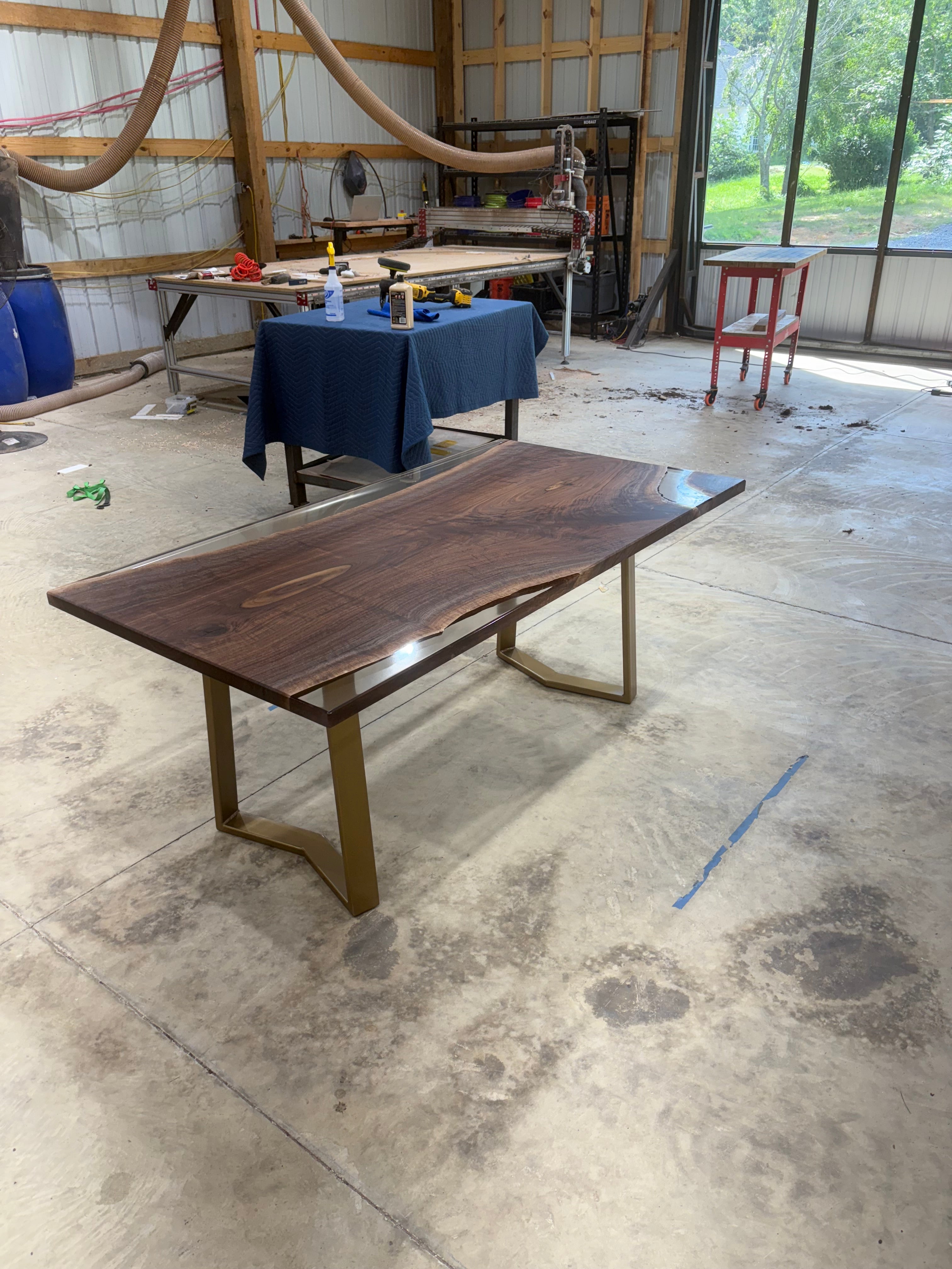 Handcrafted walnut slab table with clear resin finish and gold legs in a workshop setting