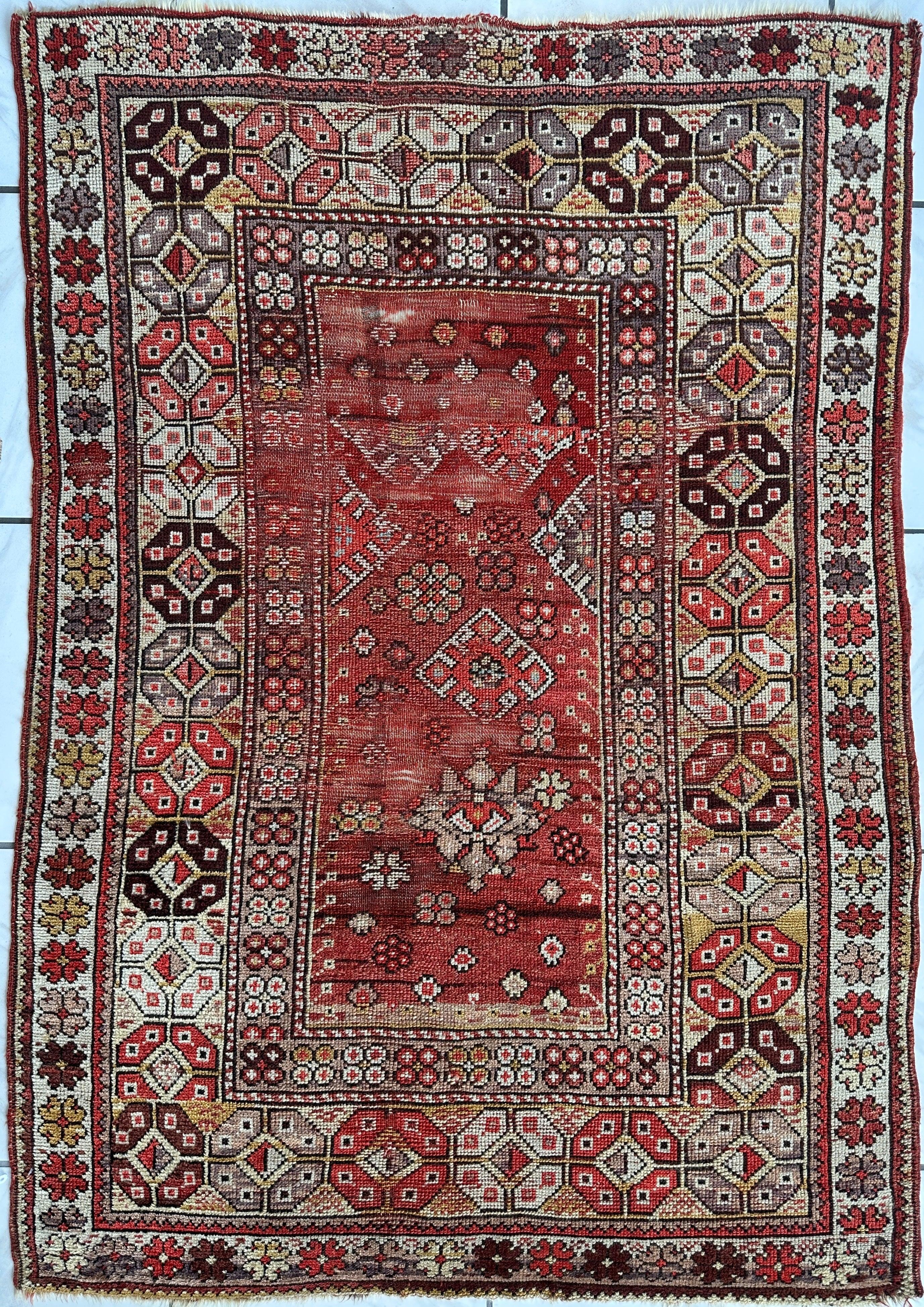 Antique Turkish hand-knotted wool prayer rug with mosque pattern in tan, gray, cream, mauve, and black on a red background, showing fringed edges and medium pile.