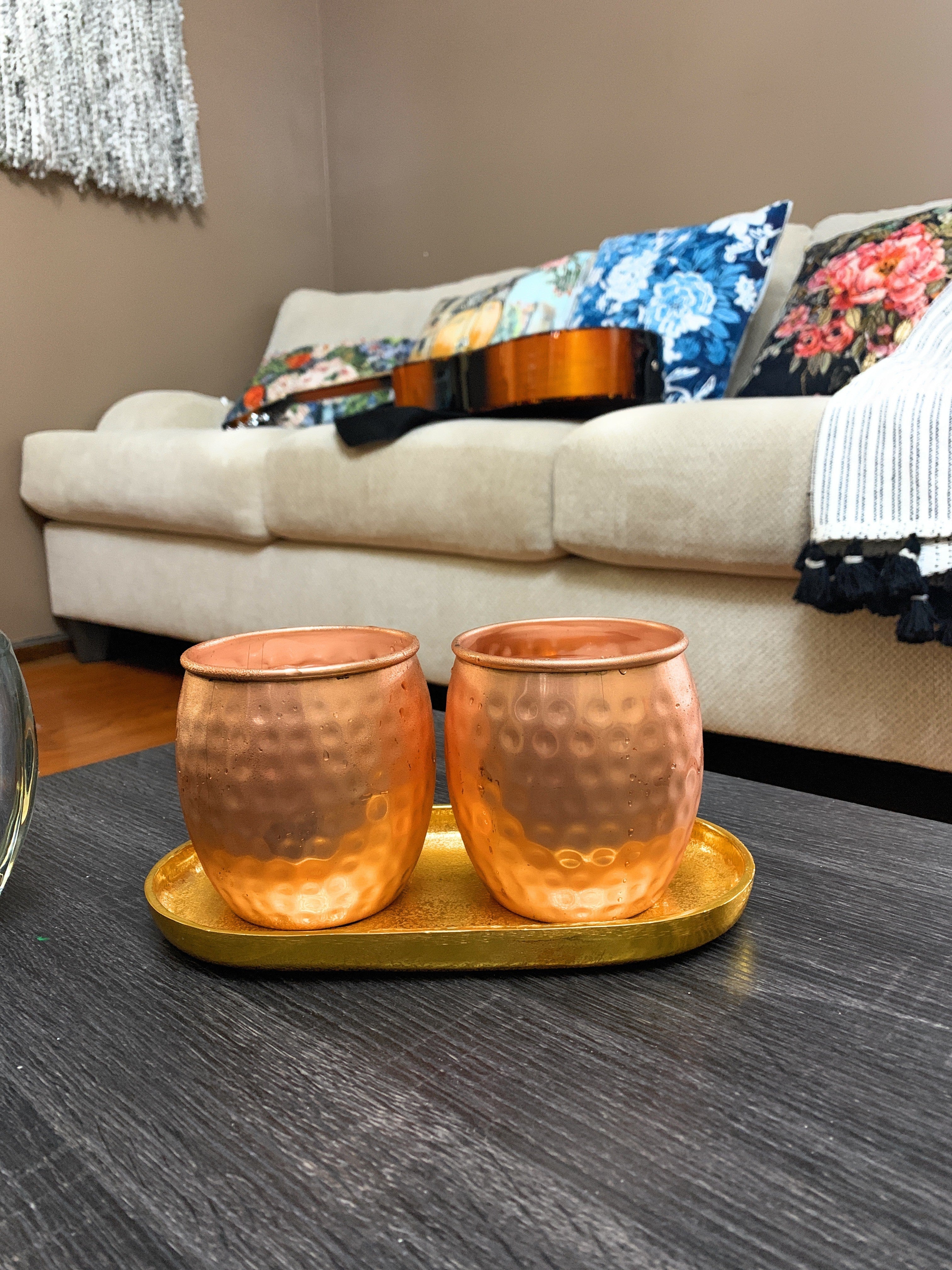 Set of four hammered copper Moscow Mule mugs with golden brass handles on a wooden surface