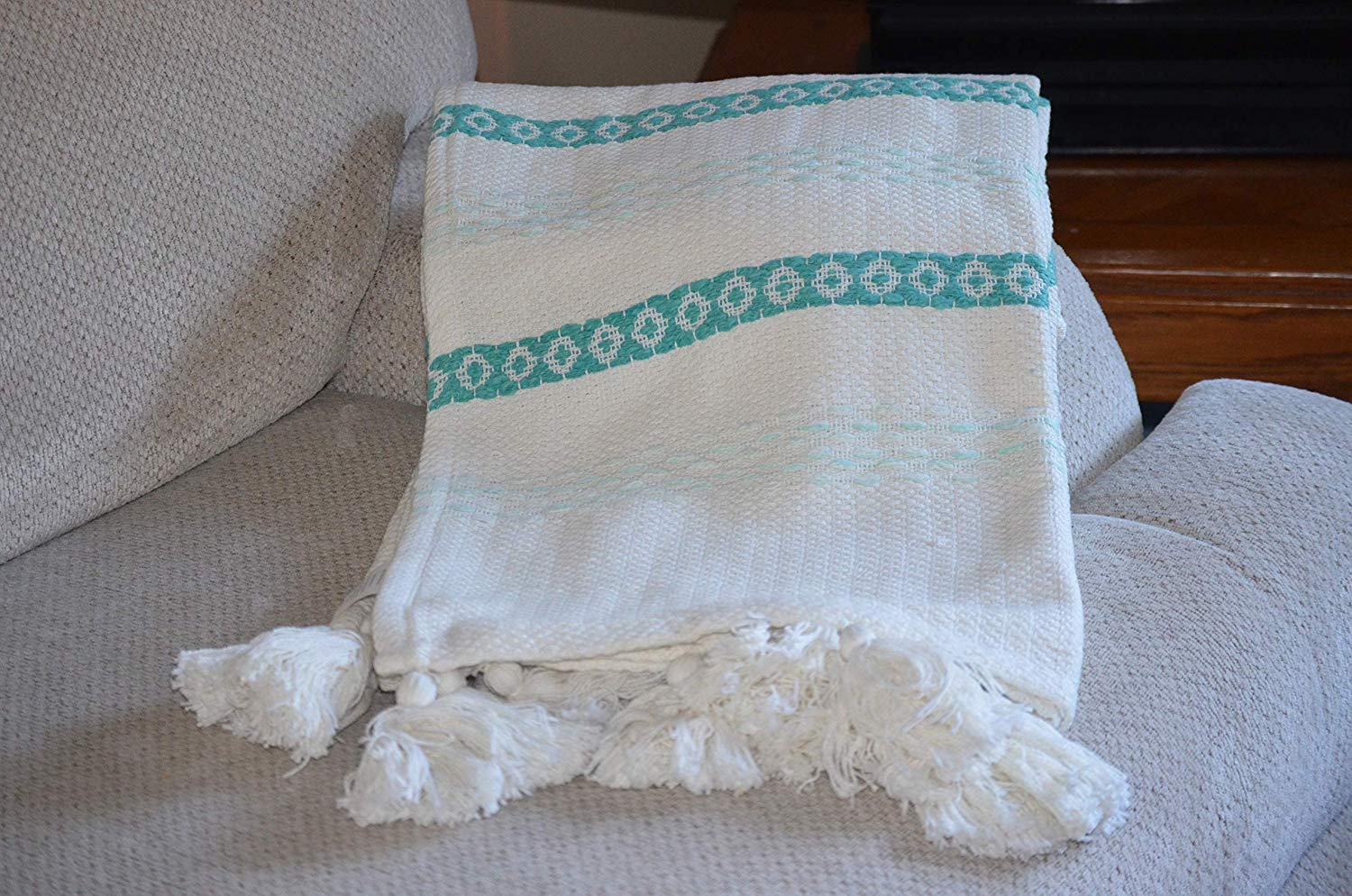 Turquoise and white hand loom woven throw with chunky tassels draped on a couch