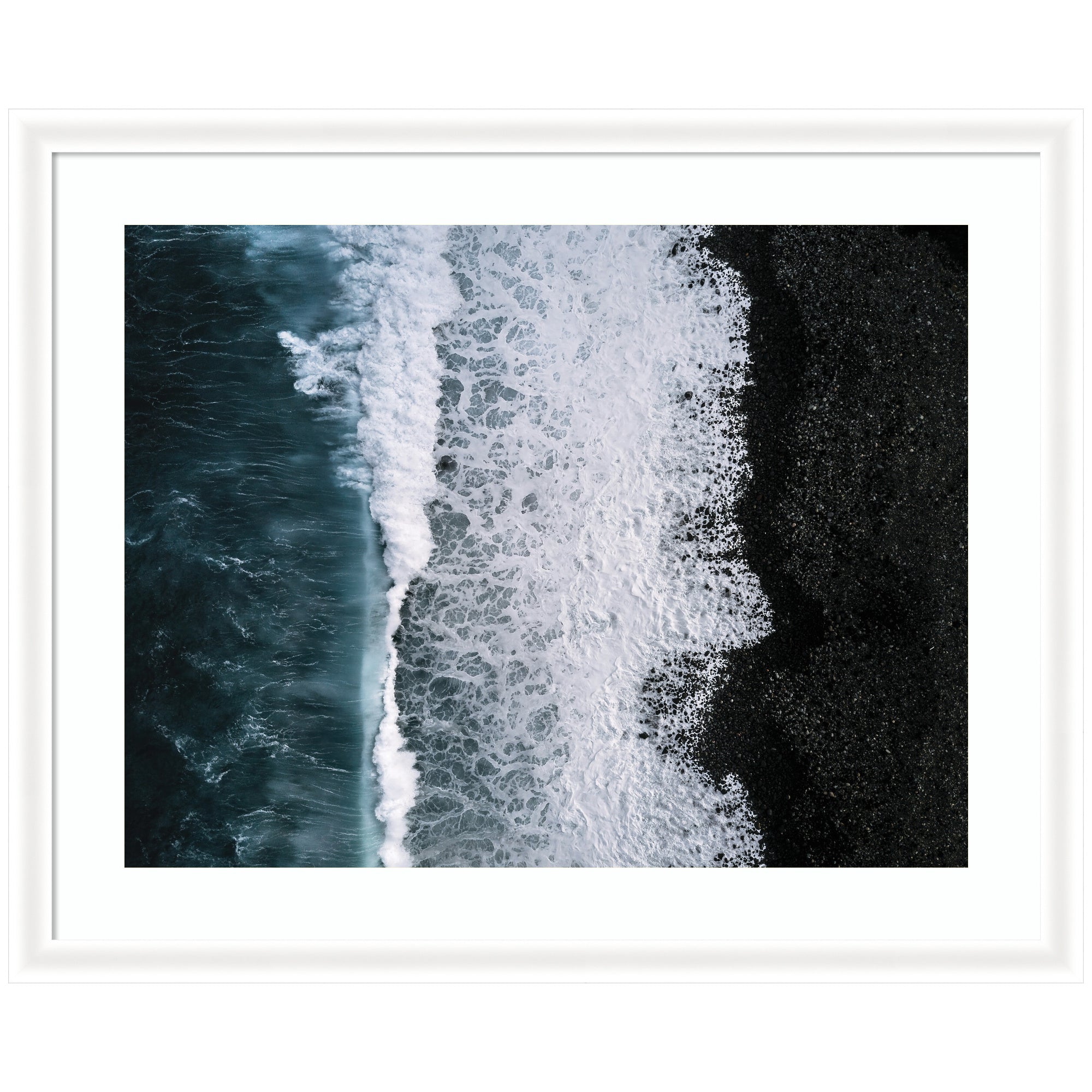 Aerial view of ocean waves crashing against a black pebble beach with white foamy patterns, framed in white narrow moulding