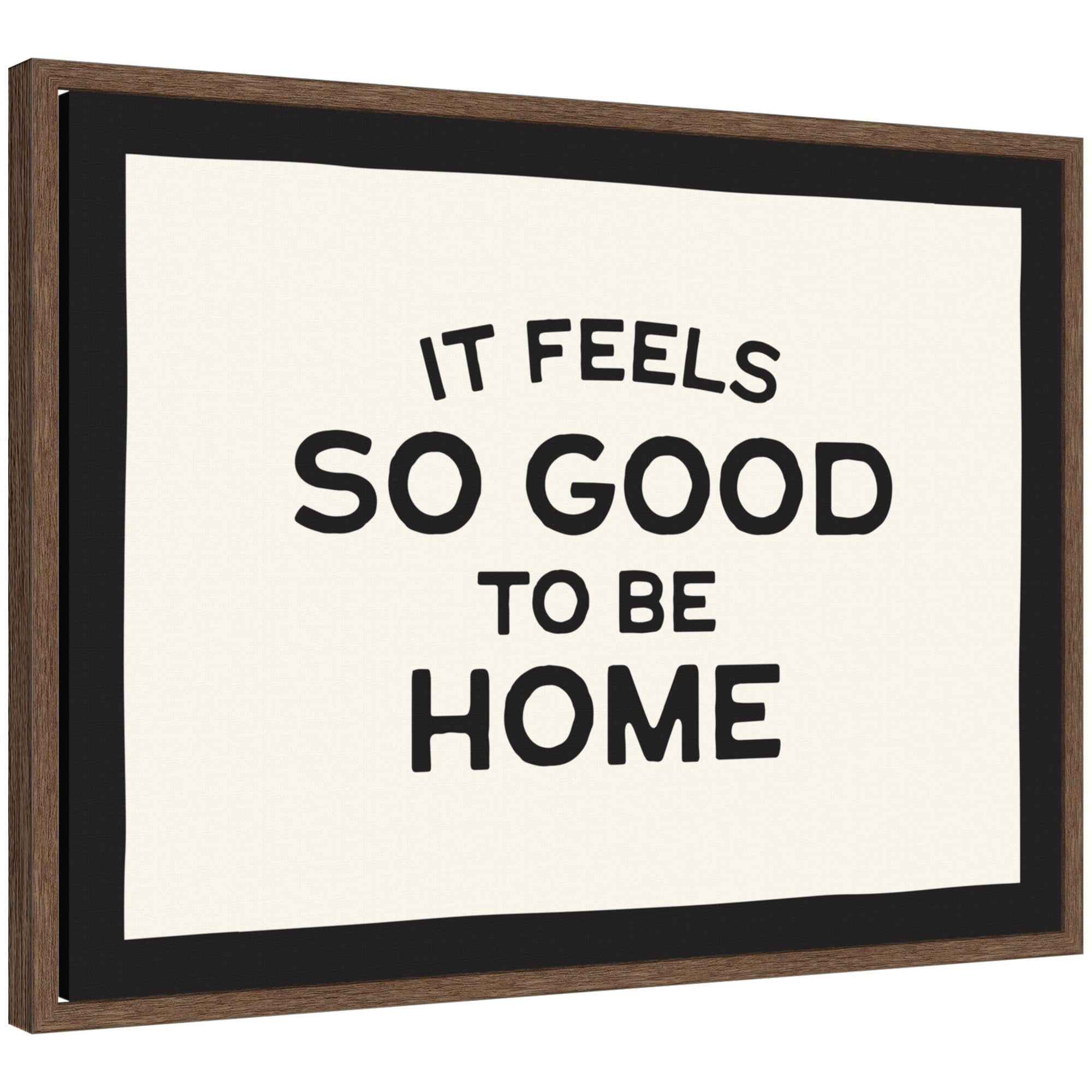 Black and white typography framed canvas art reading 'It Feels So Good to be Home' by Lucky Guava, set in a walnut brown Sylvie frame.