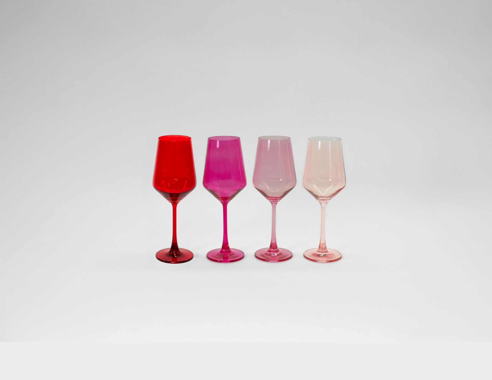 Set of four Red & Rose ombre colored wine glasses in varying pink shades from deep red to light pink, displayed on a wooden surface.