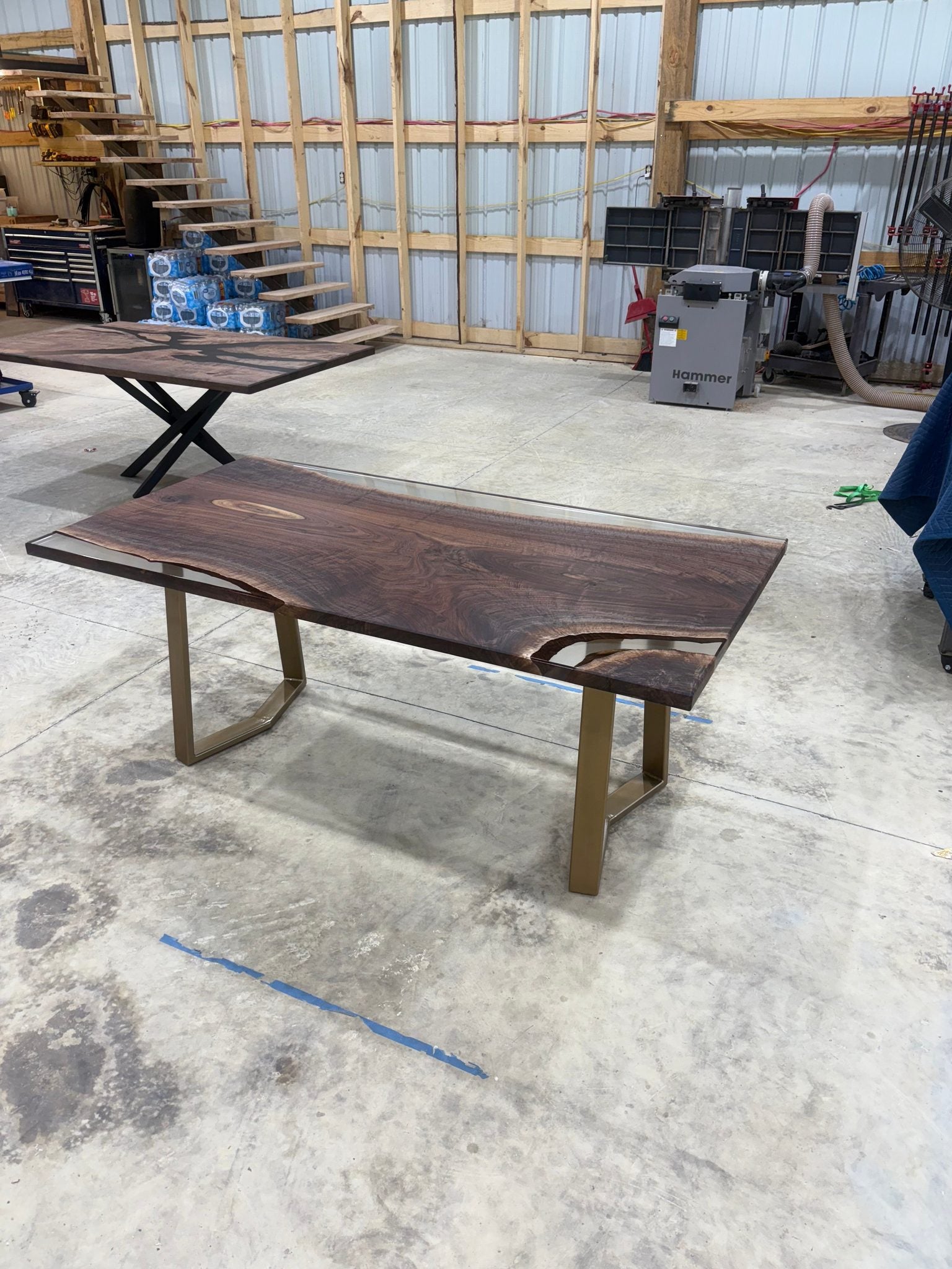 Handcrafted walnut slab table with clear resin finish and gold legs in a workshop setting