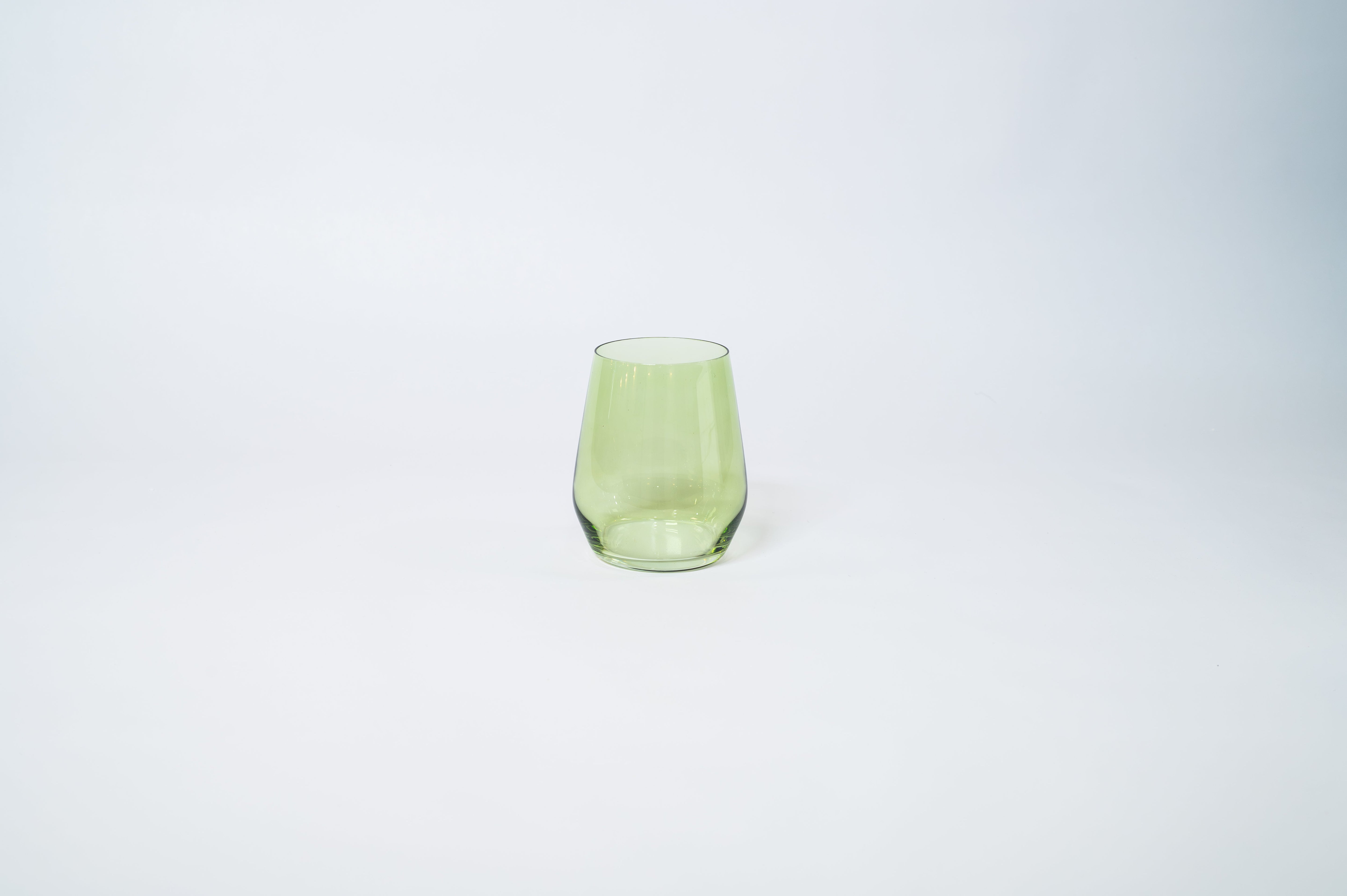 Matcha Green Stemless Colored Wine Glass from glasshauseco shown on a neutral surface with green and blue neighboring glasses