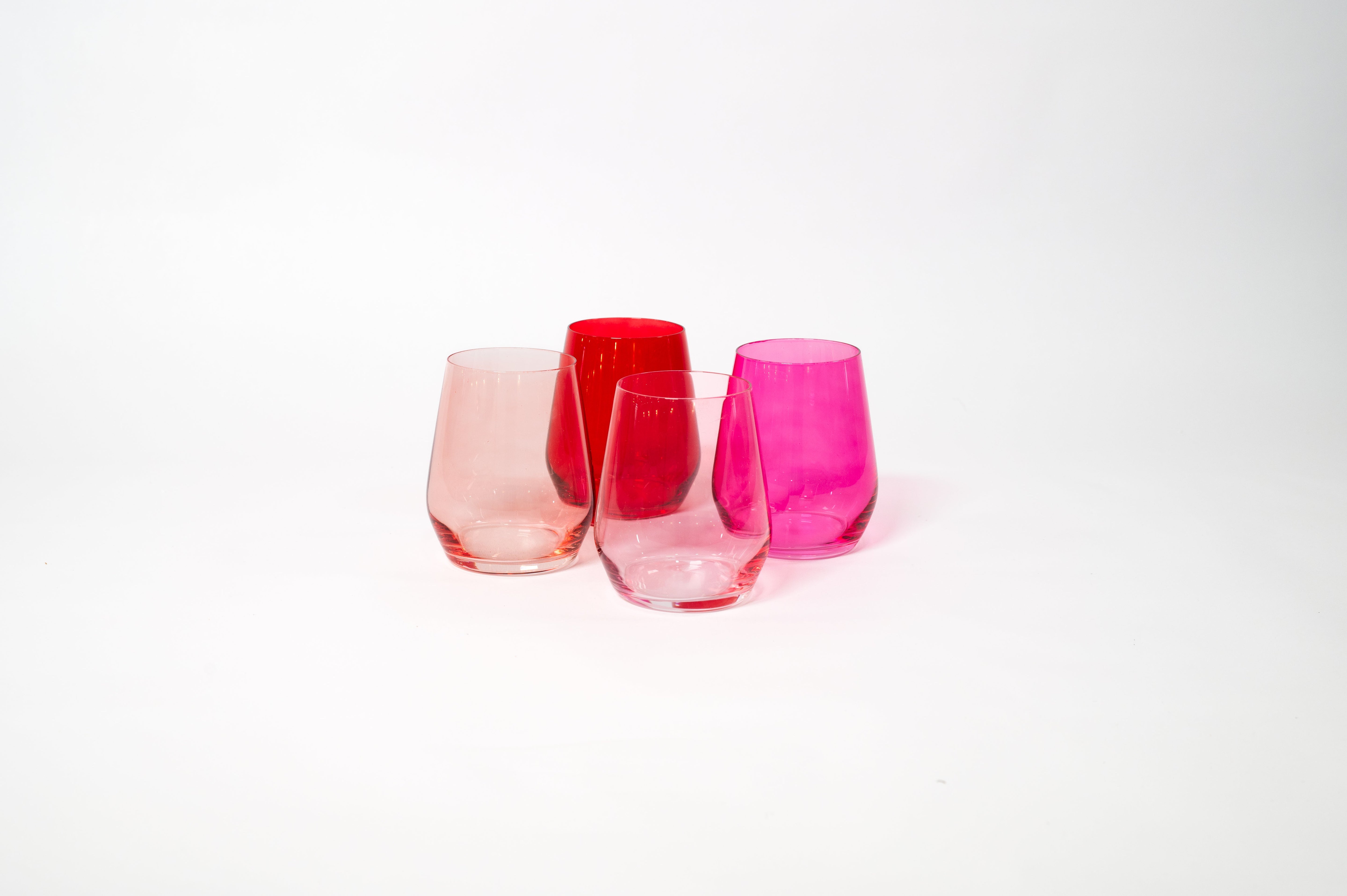Four stemless ombre wine glasses arranged in shades from dark red to soft pink on a white surface.