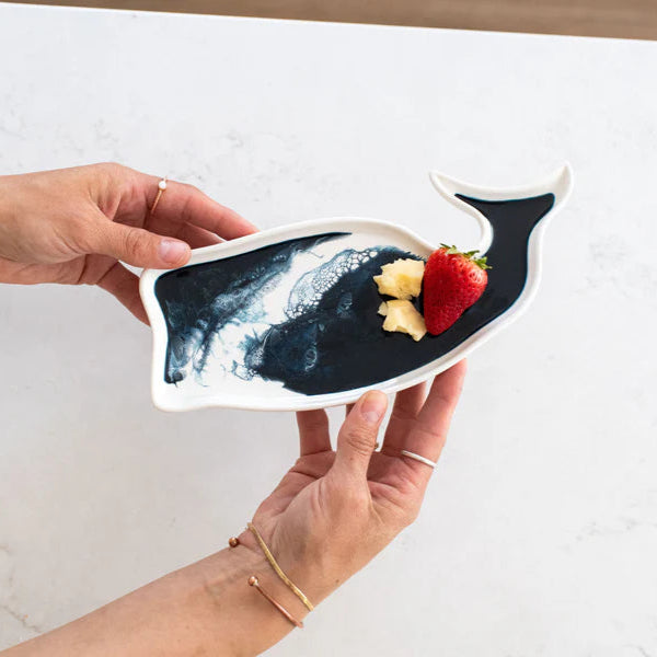 Hand holding a resin whale-shaped plate with food on a white surface