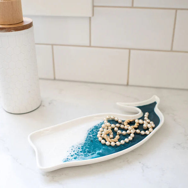 Decorative resin ceramic dish shaped like a wave on a kitchen counter with a necklace on it.