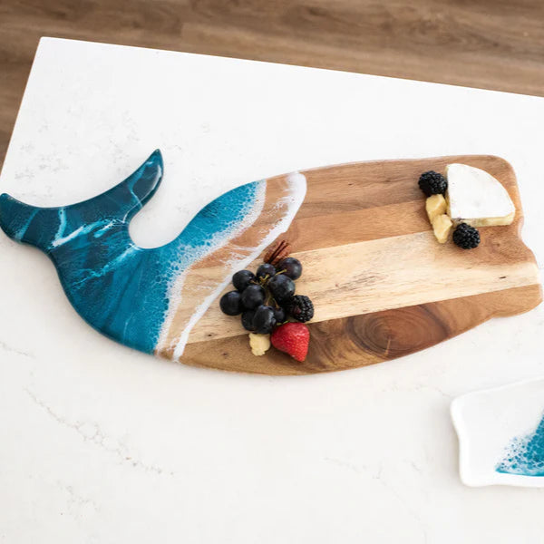 Wooden charcuterie board shaped like a whale with a blue tail on a white surface.