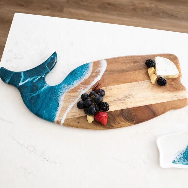 Wooden whale shaped charcuterie board shaped like a whale with a blue tail on a white surface.
