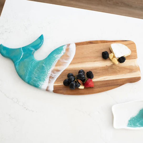 Wooden whale shaped charcuterie board with ocean-themed design on a white surface