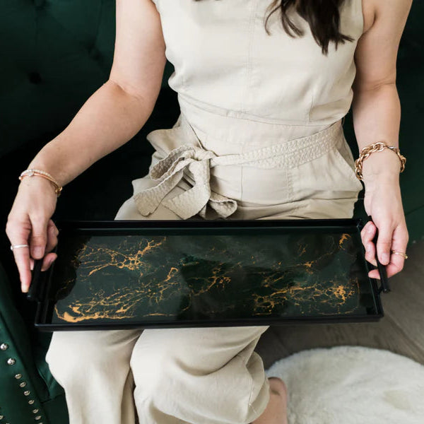 Person holding a black resin tray with gold patterns on a green couch.