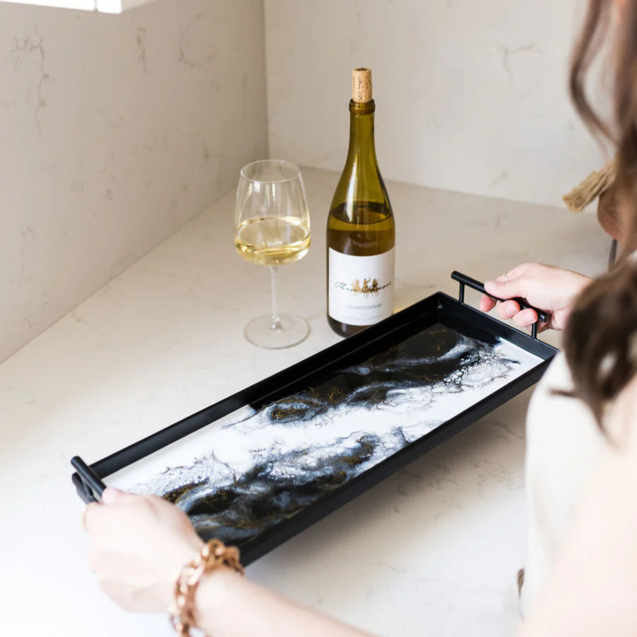 Person holding a resin tray with a bottle of wine and a glass on a kitchen counter.