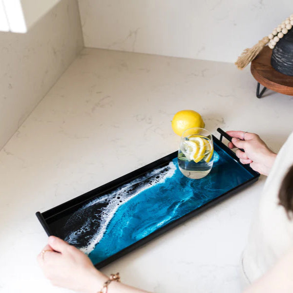 Person holding a resin tray with a drink and lemon garnish, sitting at a table.