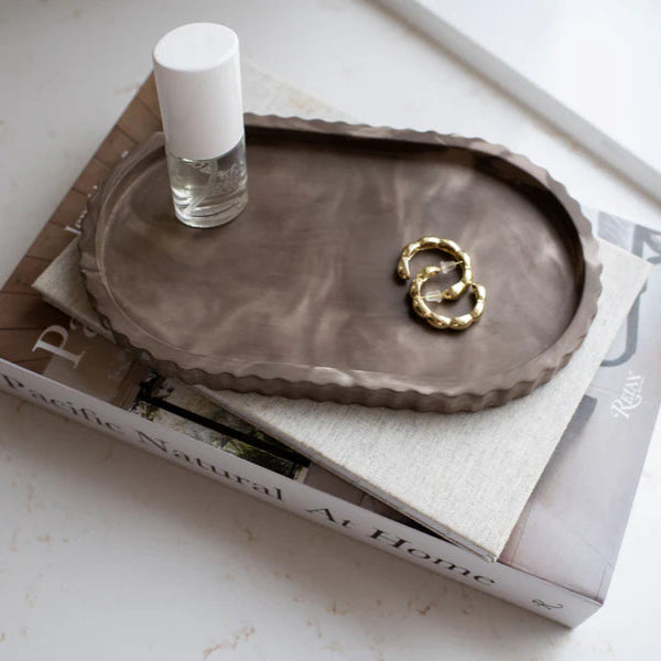 Brown ceramic tray with a gold ring and small bottle on top of a magazine
