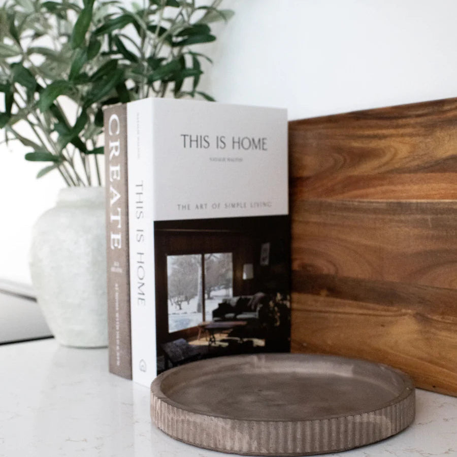 Book titled 'This is Home' by Create on a surface with a decorative plate and plants in the background.