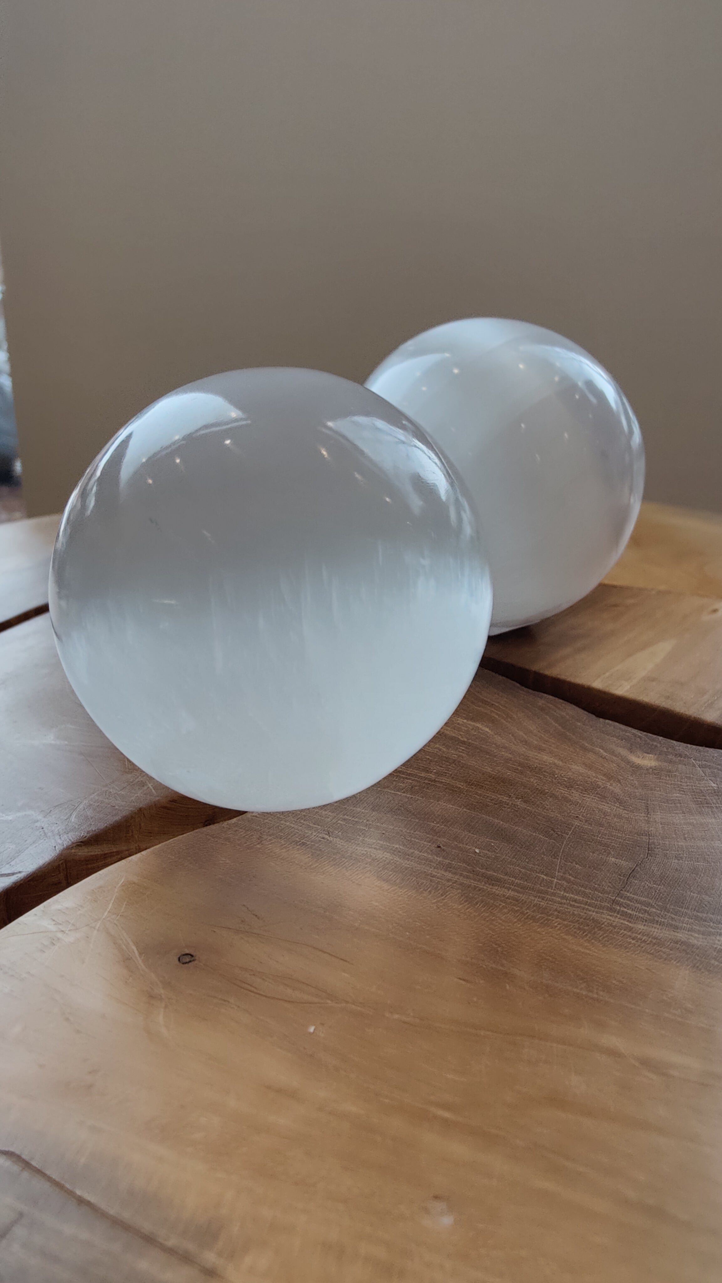 Selenite Sphere 8cm resting on a dark wooden stand with a soft glowing translucent surface