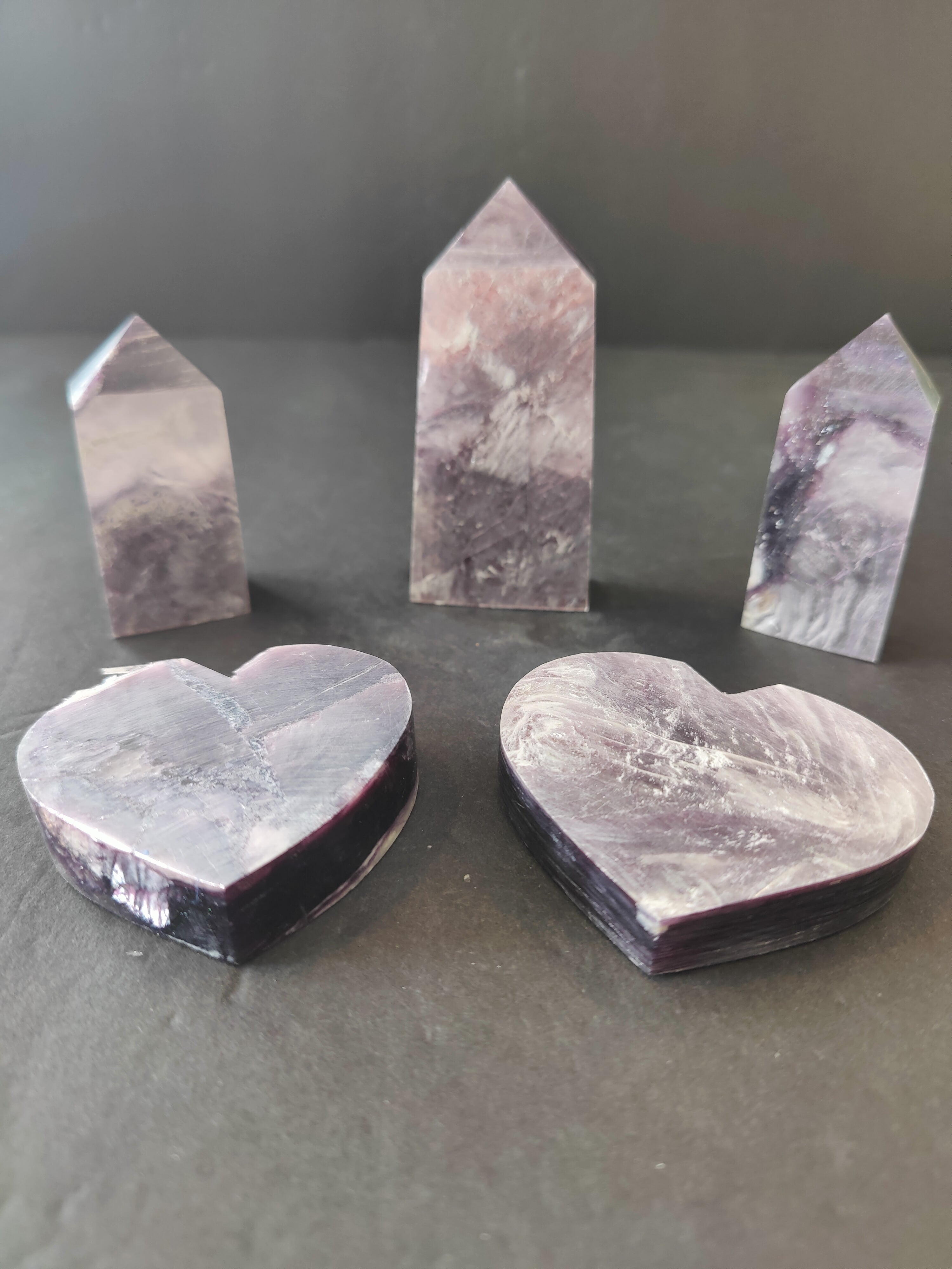 Lepidolite heart and tower sculptures with soft purple hues, displayed on a white surface with diffused light.