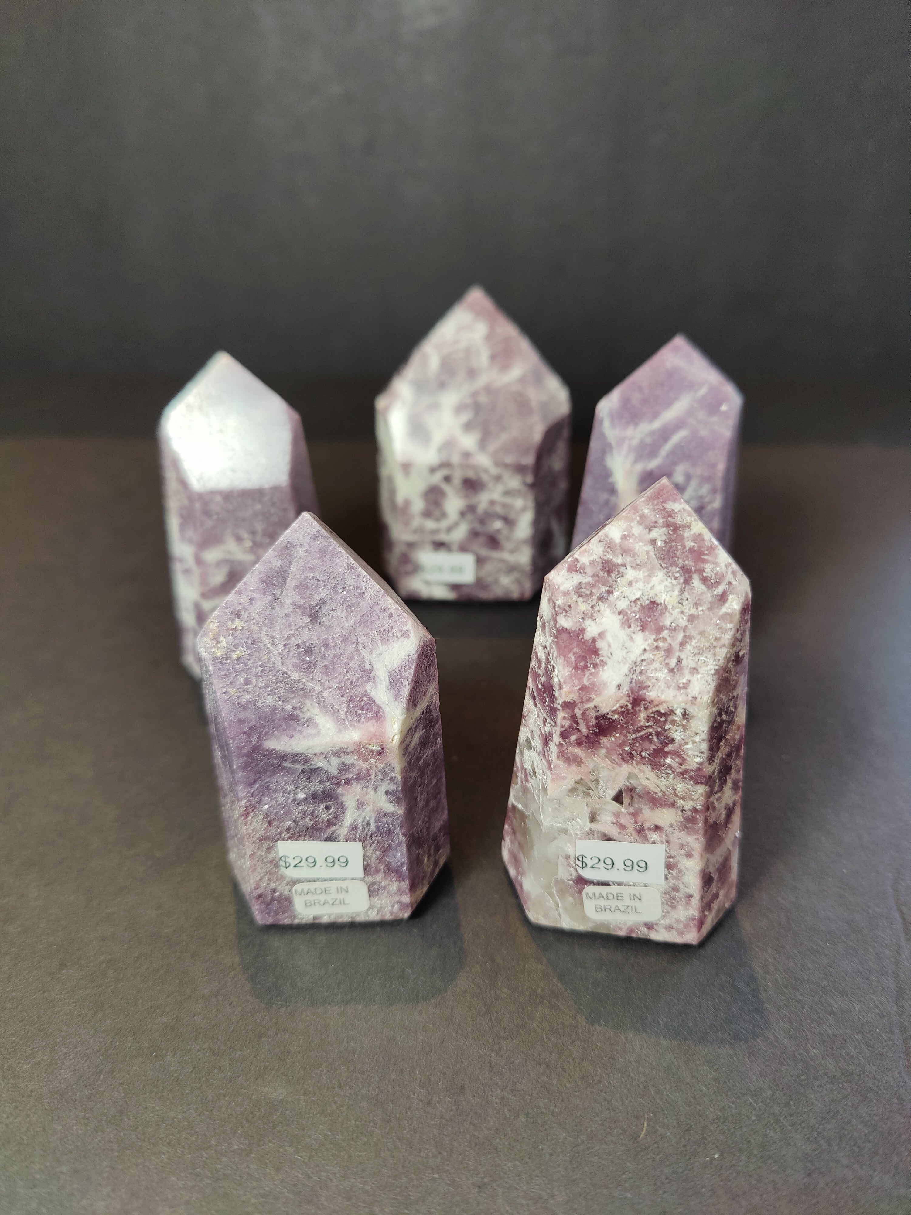 Various sizes of lepidolite polished obelisk tower sculptures, showing purple and white mineral patterns