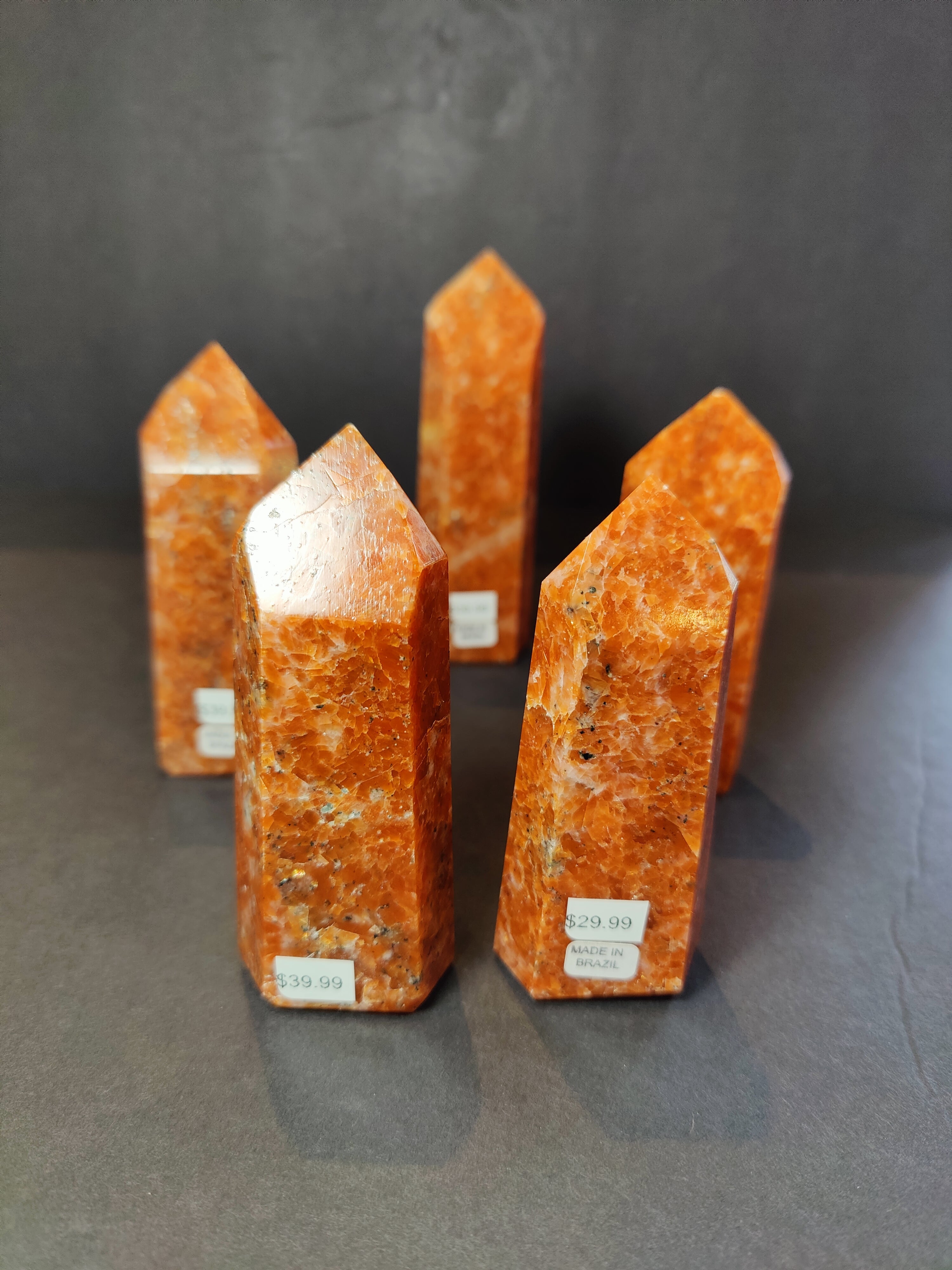 Sunstone polished obelisk tower sculpture with warm orange and golden hues on a neutral background