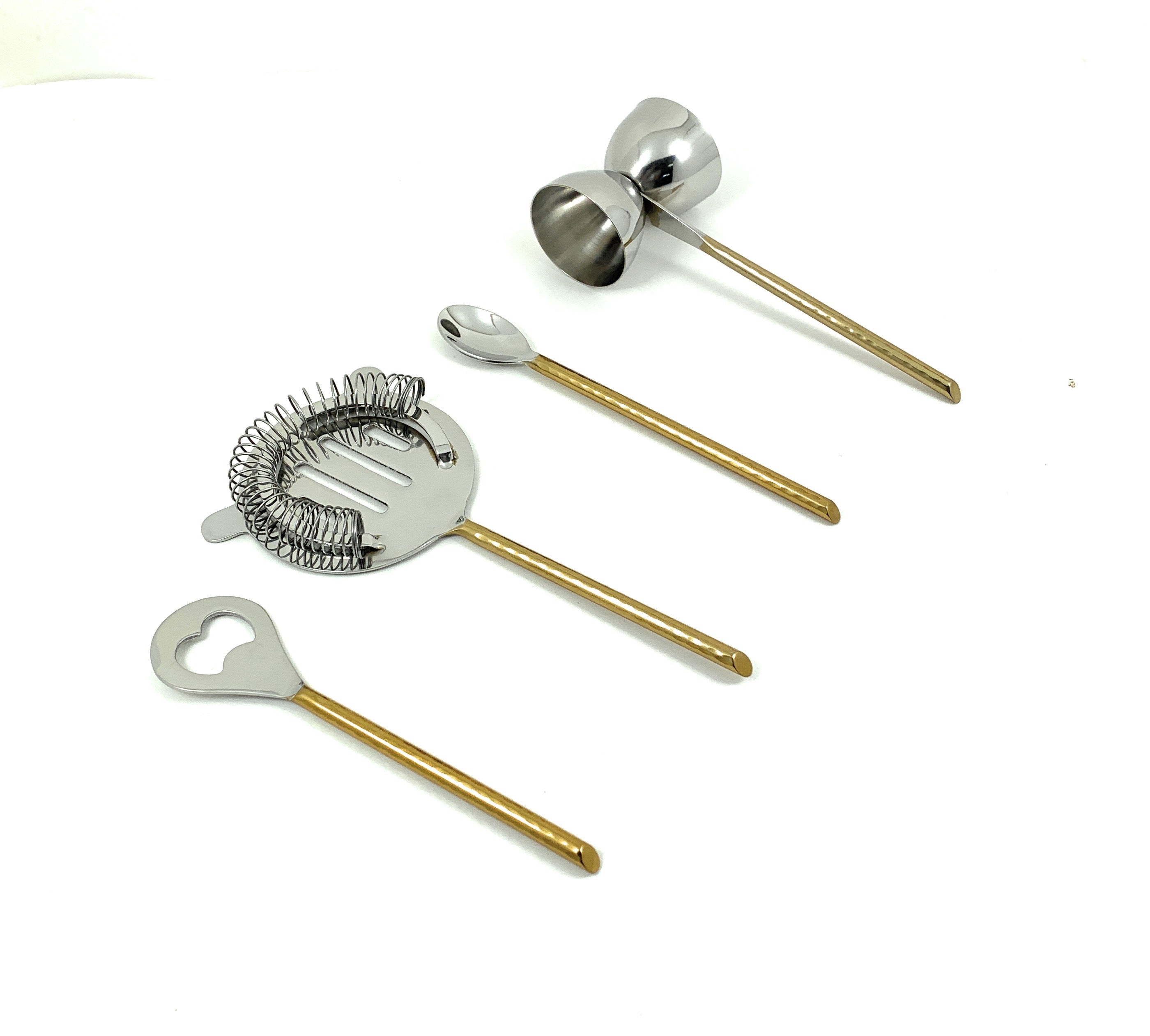 Vibhsa bar tools set with flat opener, jigger, stirring spoon, and martini shaker in golden hammered finish arranged on a dark surface