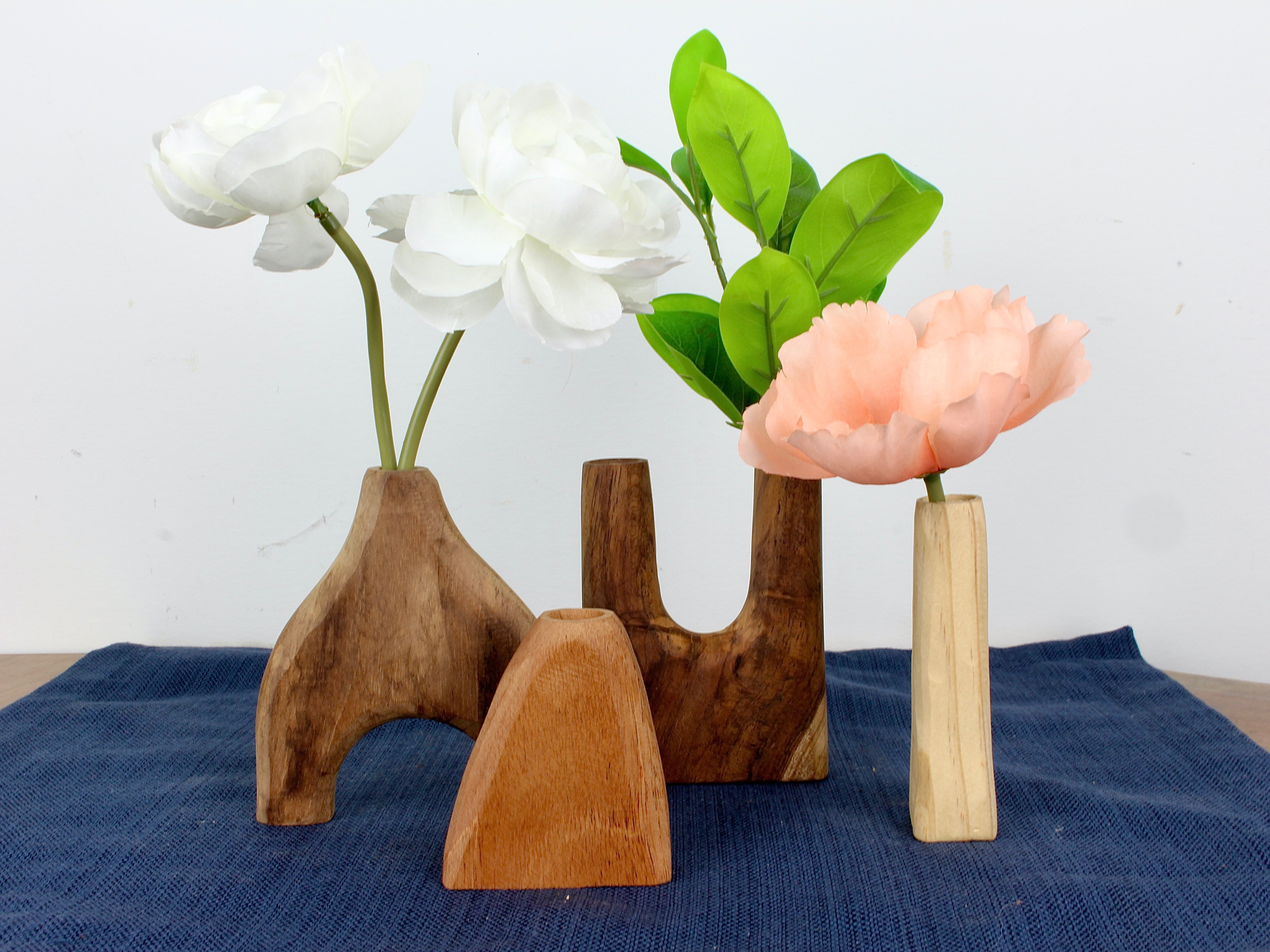 Set of four small hand carved wooden vases each of a different wood with distinct grains and shapes set on a wooden surface