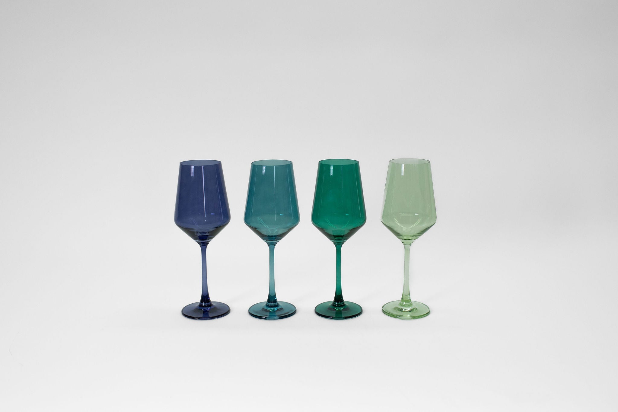 Four stemless colored wine glasses in blue and green shades set on a light surface