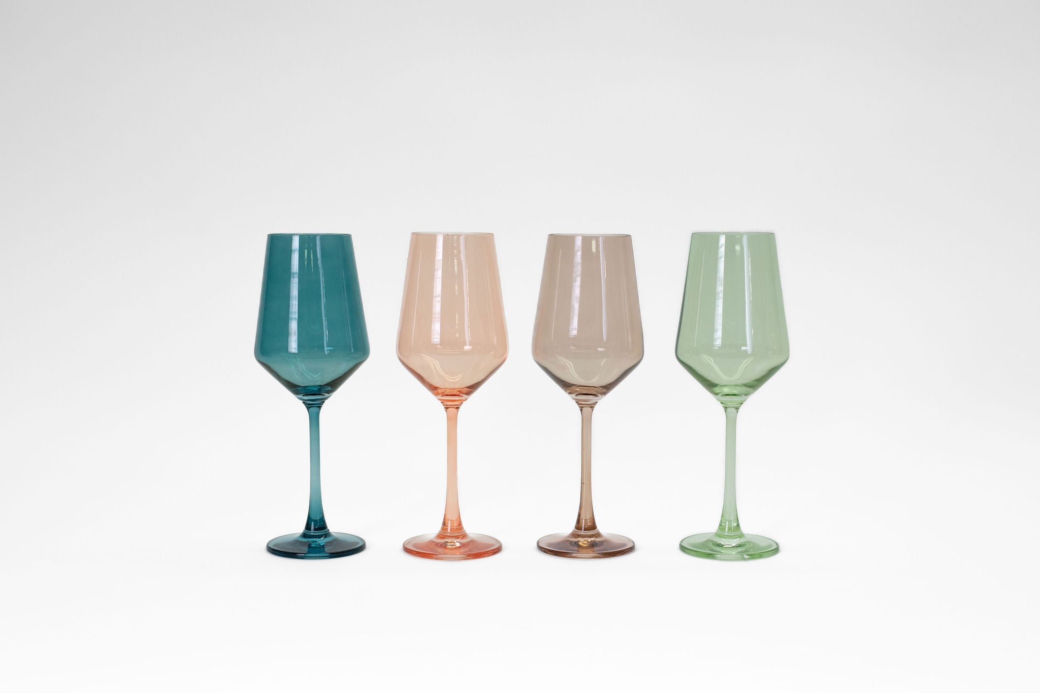 Four colored stemmed wine glasses in brown, peach, teal, and green hues from glasshauseco displayed on a table
