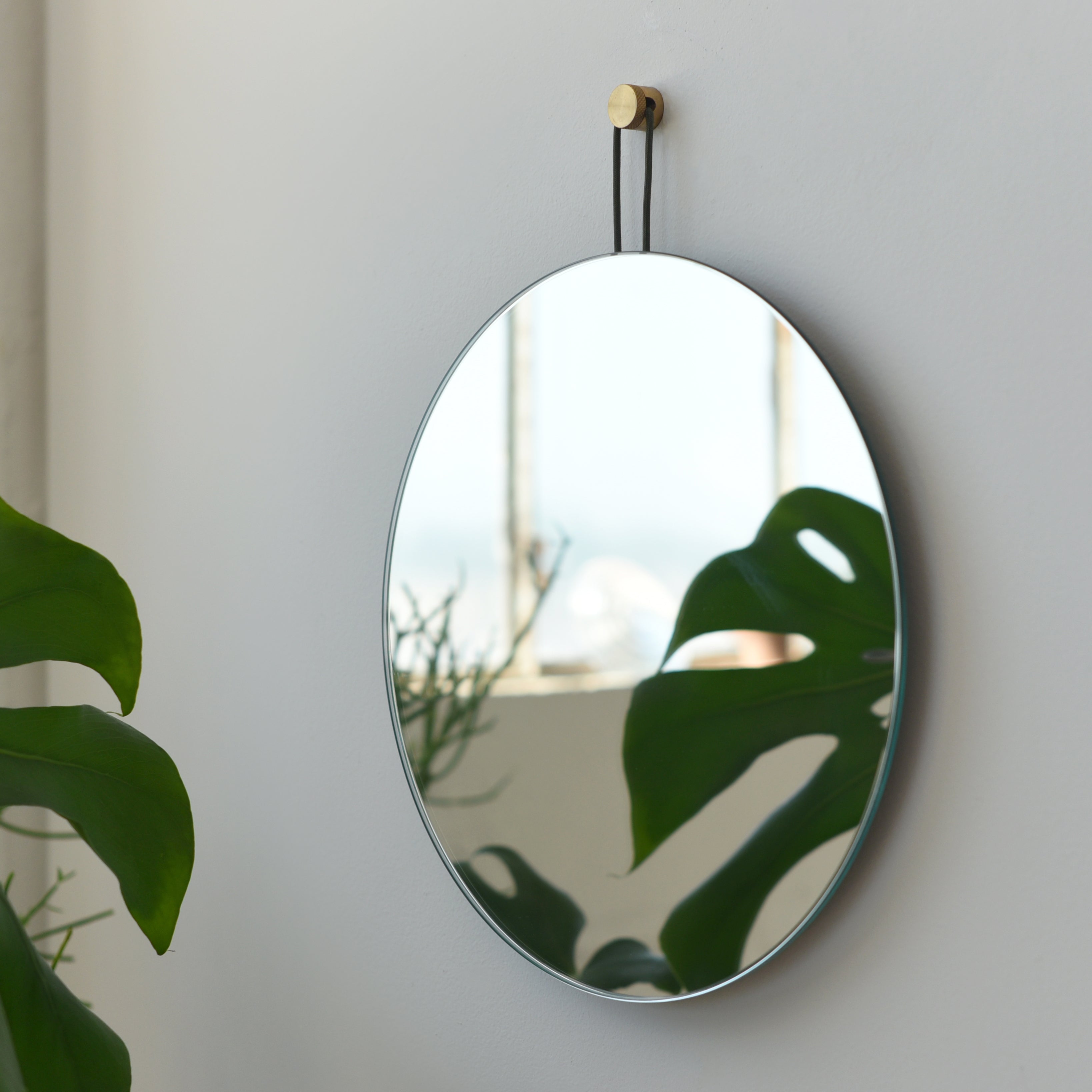 Round Lure Mirror by Misewell hung on a muted grey wall next to minimal decor