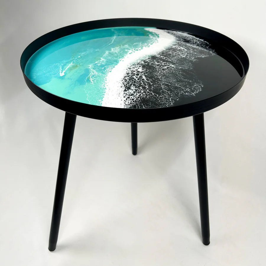 Round resin table with a black rim and legs, featuring a design of ocean waves on the top.