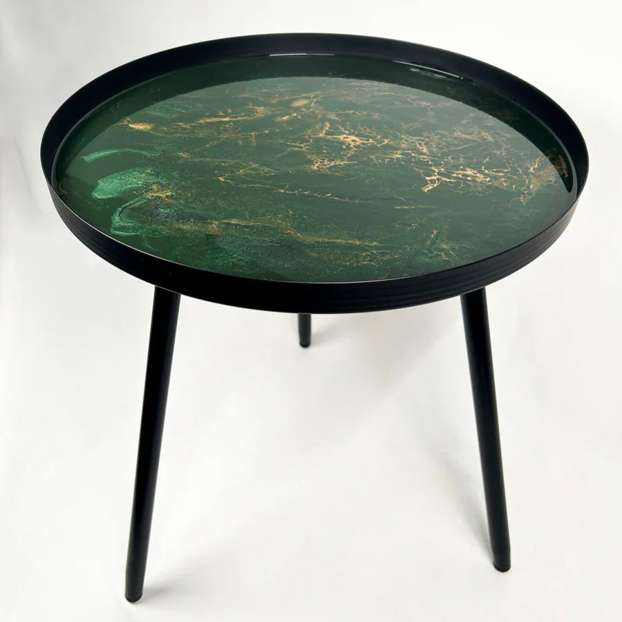 Round small resin side table with green marbleized top and black legs on a white background