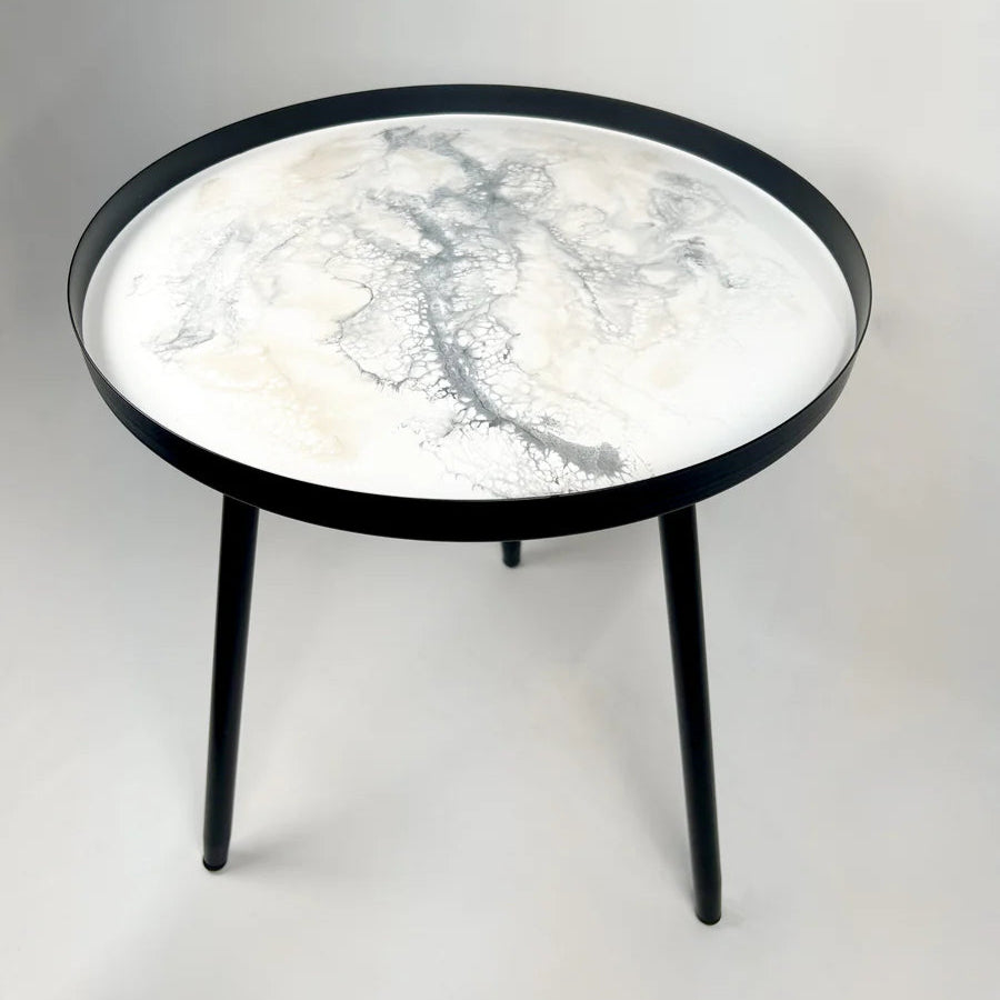 Round resin table with marble-like top and black frame on a white background