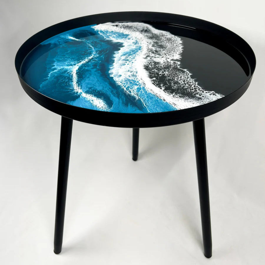 Round resin table with a design of blue and white waves on a black rim against a white background