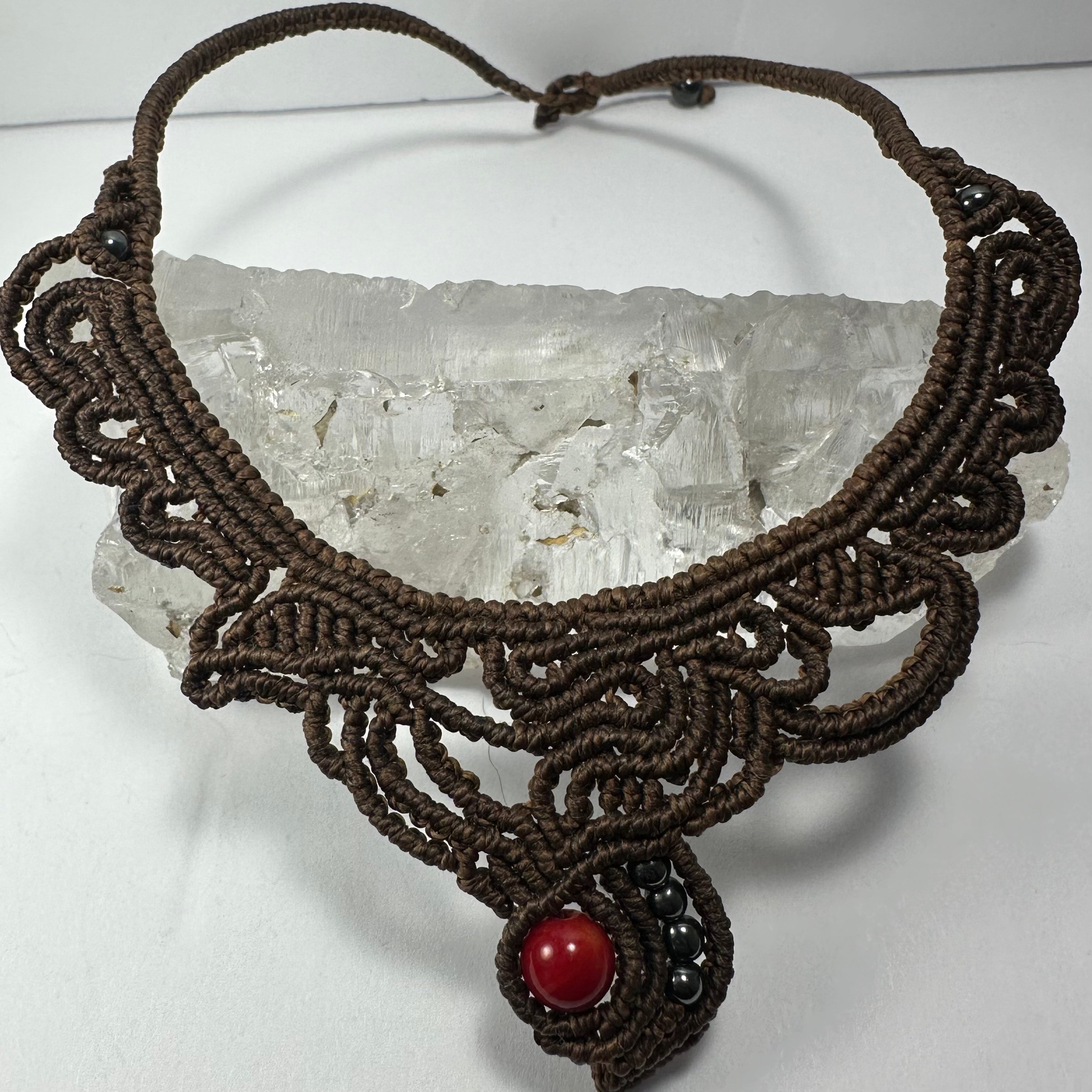Handmade macrame choker with coral bead on black fabric background