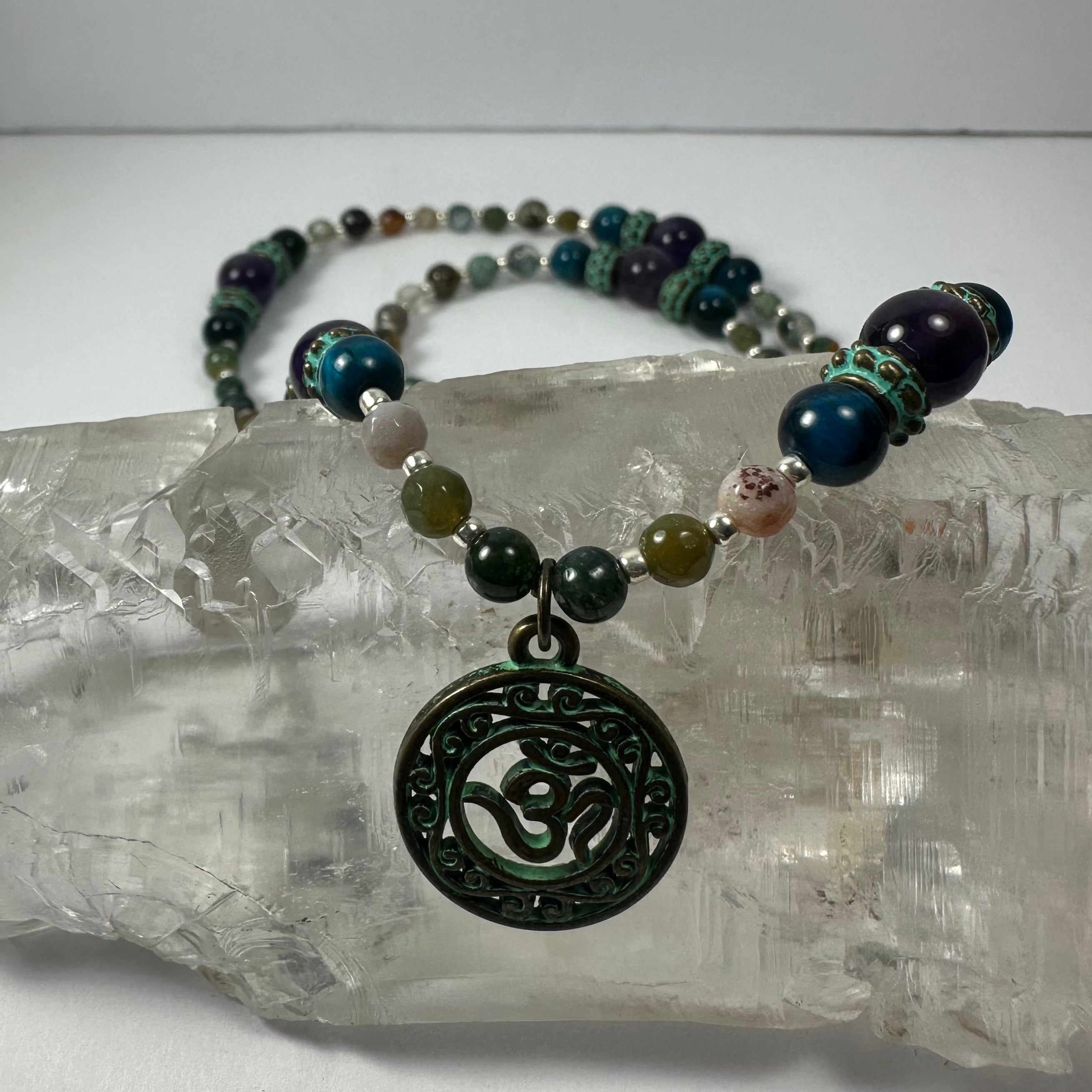 Close-up of Bronze Patina 'Om' pendant with Blue Tiger Eye and Indian Agate beads on necklace
