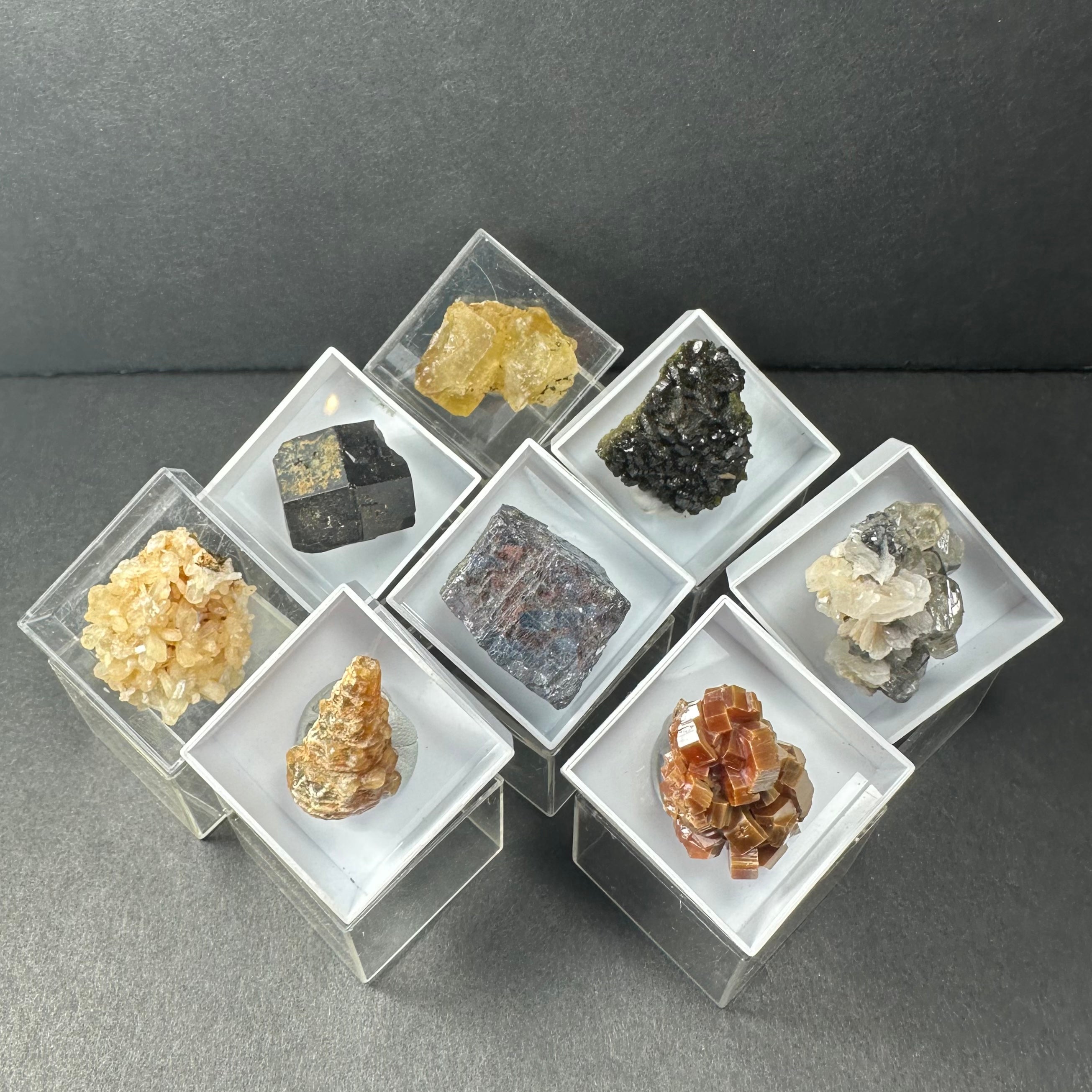 Thumbnail mineral specimens displayed in small clear acrylic boxes, each showing individual Moroccan minerals with varied colors and textures.