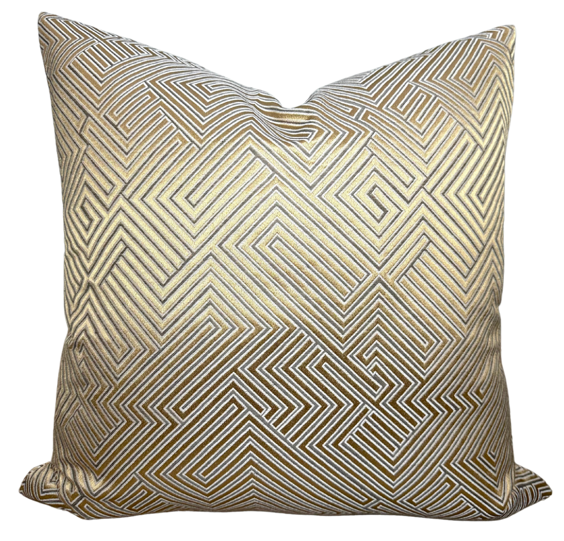Golden velvet pillow cover with geometric maze pattern displayed on a dark couch
