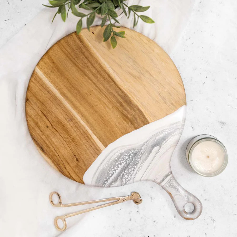 Round wooden Cheese Paddle Acacia Serving Charcuterie Board on a marble surface with a candle and plant