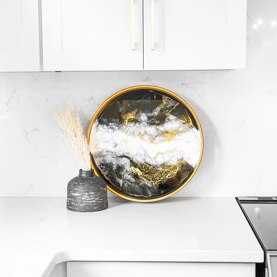 Decorative round resin serving tray with gold and black design on a kitchen counter.