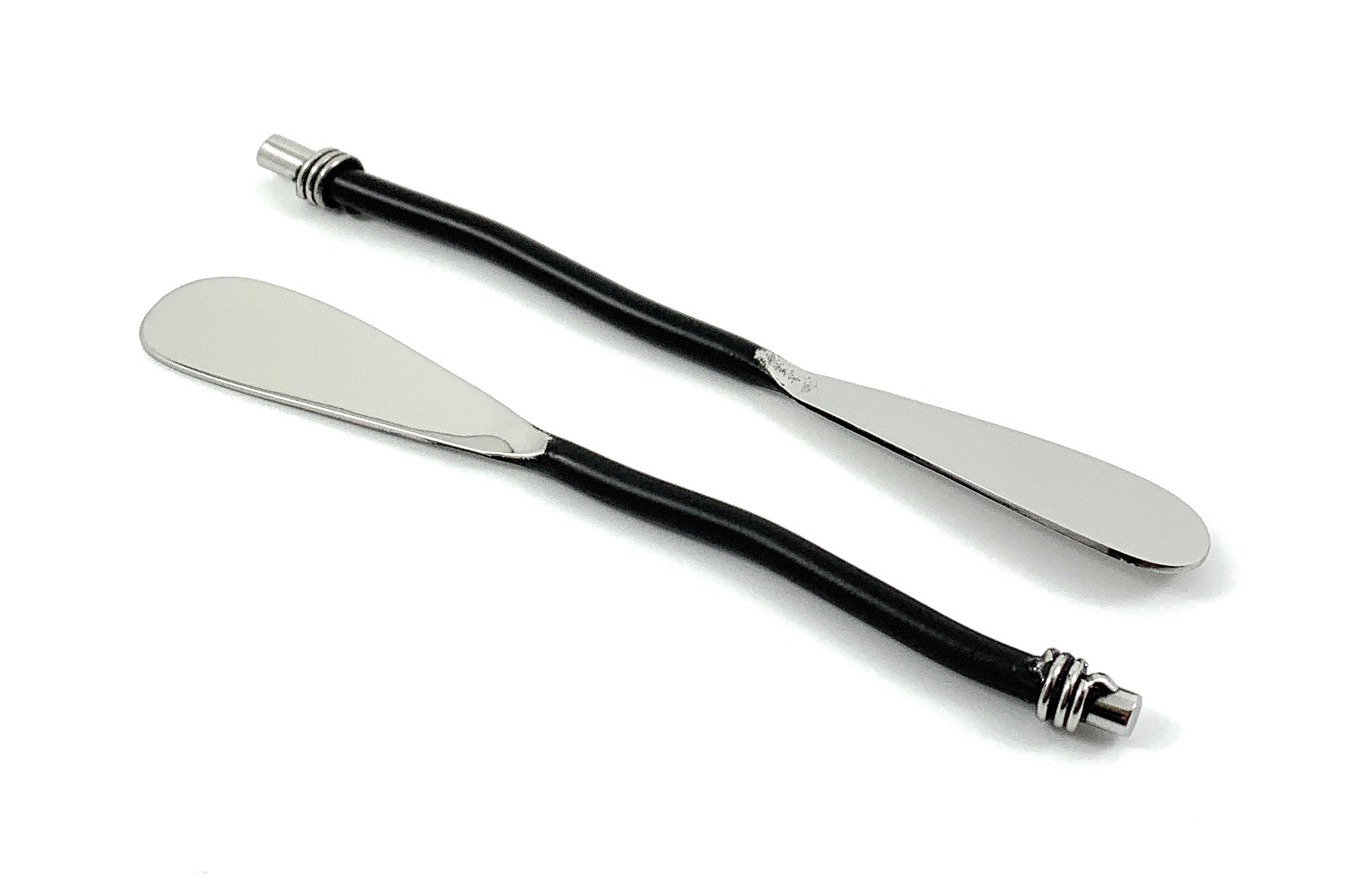 Set of six Vibhsa black silverware butter spreaders resting on a wooden surface alongside cheese and crackers