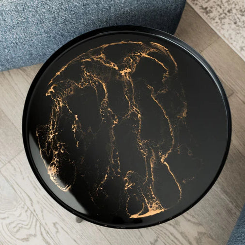 Round black small resin table with gold leaf design on a wooden floor.