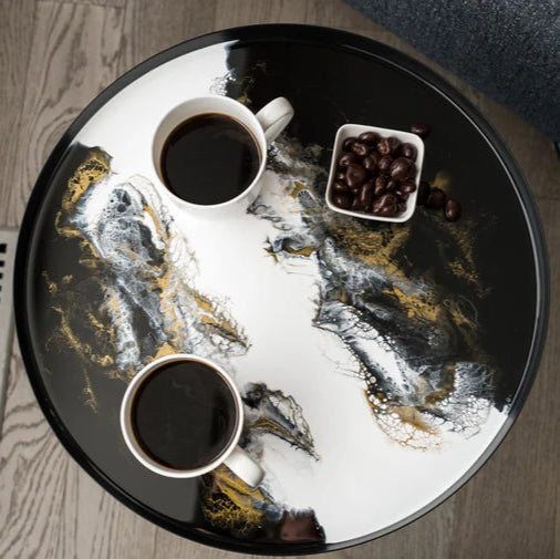 Round resin black tray with coffee cups and beans on a wooden floor.