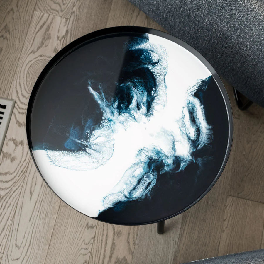 Round stool with a resin black and white abstract design on a wooden floor.