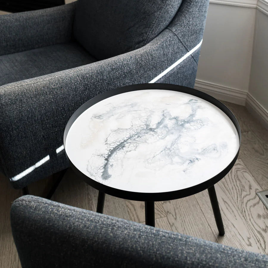 Gray armchair with a round marble resin table in a room with a fireplace and window.