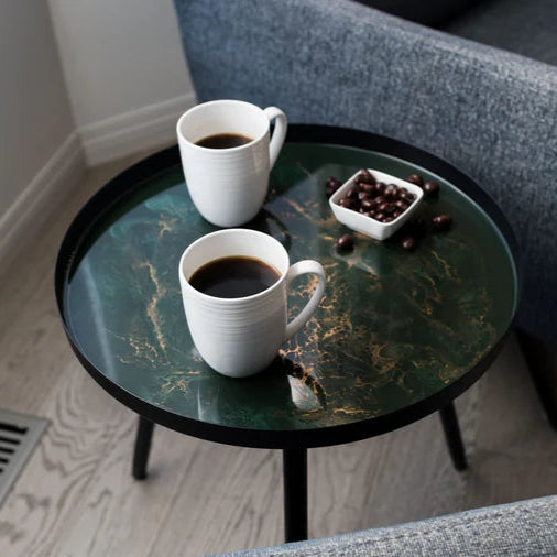 Two white coffee cups on a small round resin side table with a gray sofa in the background.